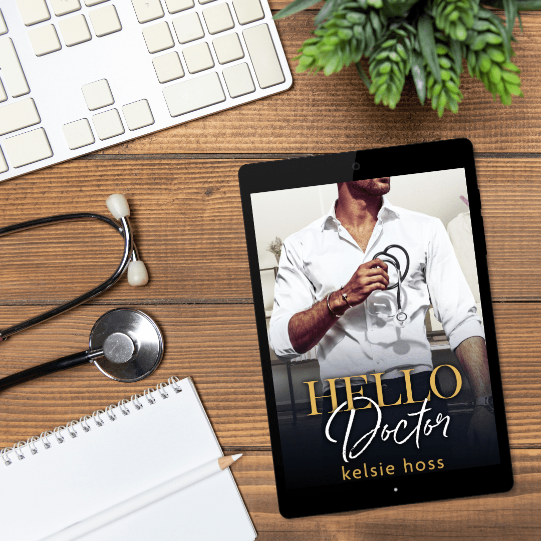 A desk background with a planet, keyboard, a stethoscope and a notebook sit near an eBook cover with an attractive man holding a stethoscope called "Hello Doctor" by Kelsie Hoss