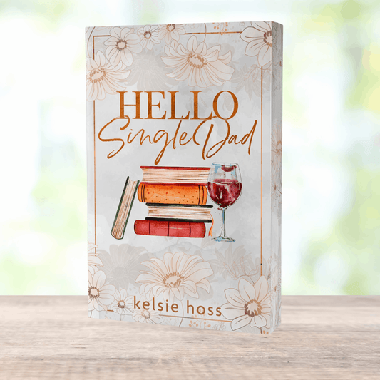 a paperback copy of Hello Single Dad by Kelsie Hoss, the cover features a stack of books next to a wine glass