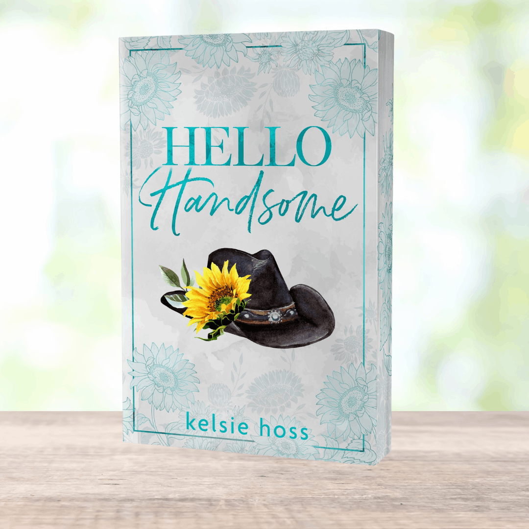 a paperback copy of Hello Handsome by Kelsie Hoss, the cover features a cowboy hat with a sunflower attached 