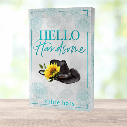 a paperback copy of Hello Handsome by Kelsie Hoss, the cover features a cowboy hat with a sunflower attached 