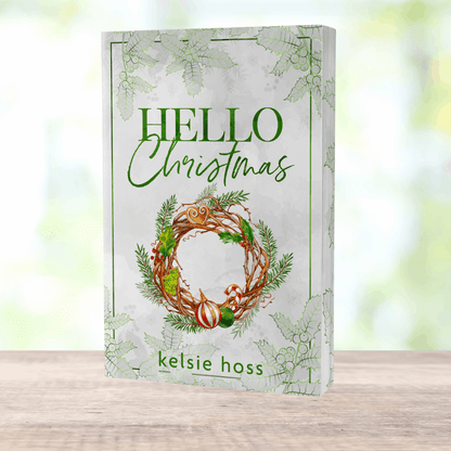 a paperback copy of Hello Christmas by Kelsie Hoss, the cover features a large golden wreath 