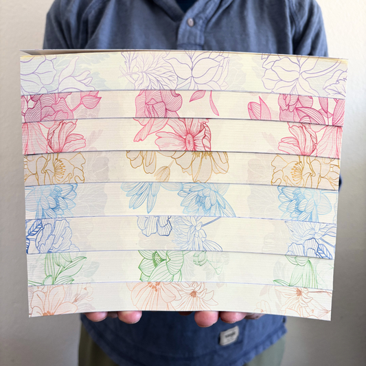 a stack of books being held up, showing the edges designed with multicolored floral designs