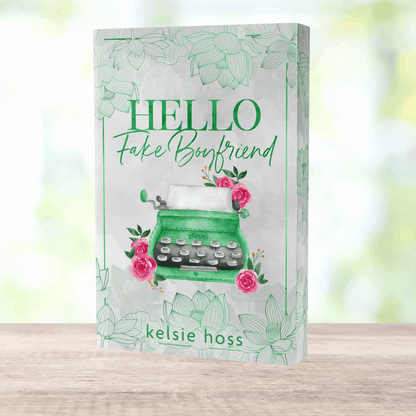 a paperback copy of Hello Fake Boyfriend by Kelsie Hoss, the cover features a green typewriter 