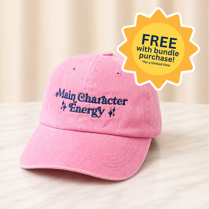 Pink cap with 'Main Character Energy' text and a promotional badge on a light background