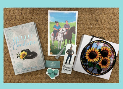 A rustic background with a light blue background displays several items. A book to the left titled Hello Handsome by Kelsie Hoss, it's cover decorated with a cowboy hat adorned with a sunflower. To its right is a heart sticker, an artistic representation of a photo of two characters, a tassel book mark and a piece of jewelry with a sunflower design