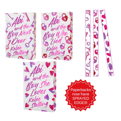 A promotional image showcasing the physical paperback editions of the series.

Layout: The three book covers are displayed as physical paperbacks. To the right, there are three vertical strips showing the decorative patterns used for the book edges.

Key Feature: A red jagged seal in the bottom right corner contains the text: "Paperbacks now have SPRAYED EDGES!"

Design Details: The patterns on the edges match the motifs of the covers: keys for the first book, heart-shaped padlocks for the second, and float